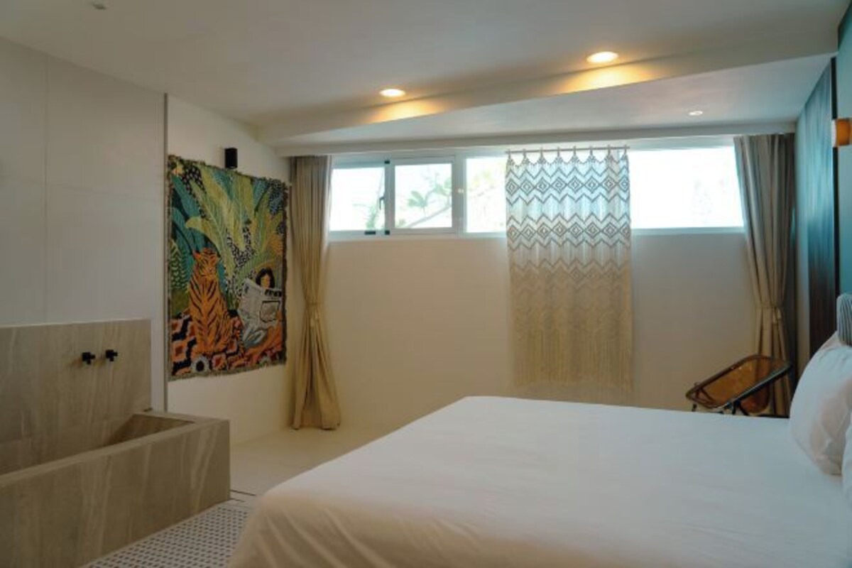 A hotel room with a large bed, a window with curtains, a wall-mounted artwork, and a small seating area.
