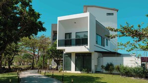 Un edificio moderno a due piani con ampie finestre e tetto piatto, immerso nel verde e con un vialetto lastricato.