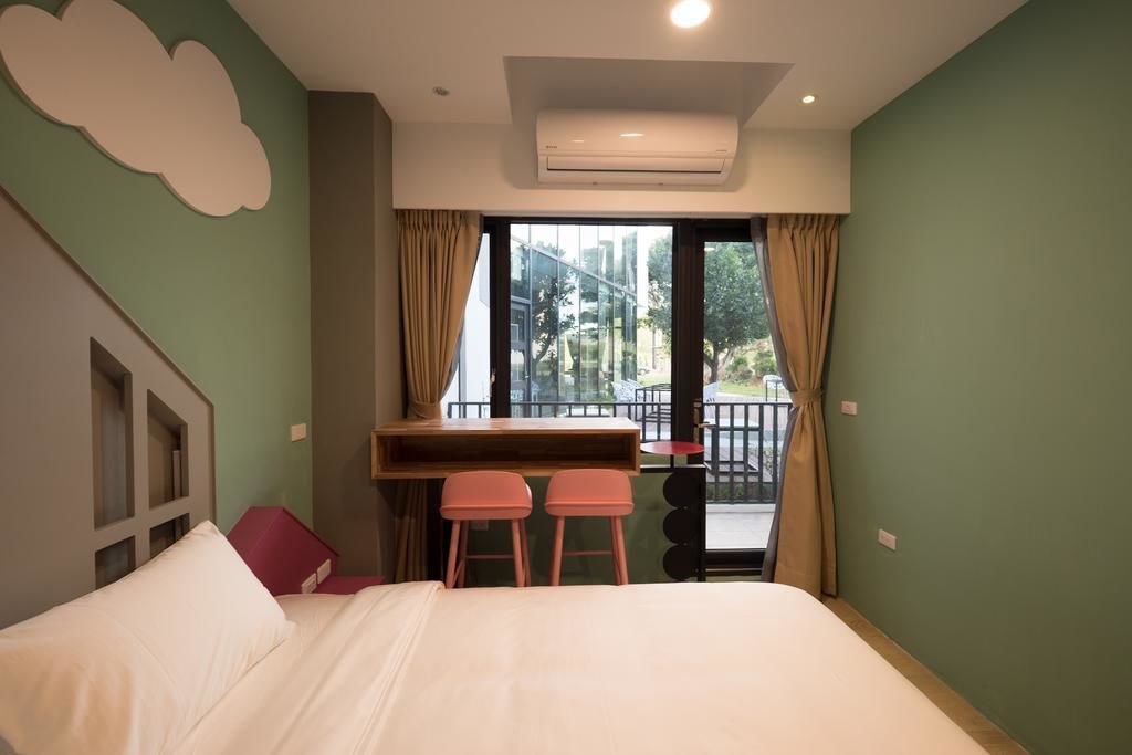 Quarto de hotel com cama, secretária e duas cadeiras, janela com cortinas e unidade de ar condicionado.