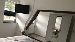 A bedroom with two beds, a wardrobe, a television, and a window with blinds.