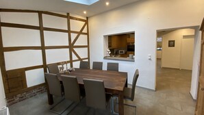 A modern dining area with a wooden table and chairs, a skylight, and a view of a kitchen.