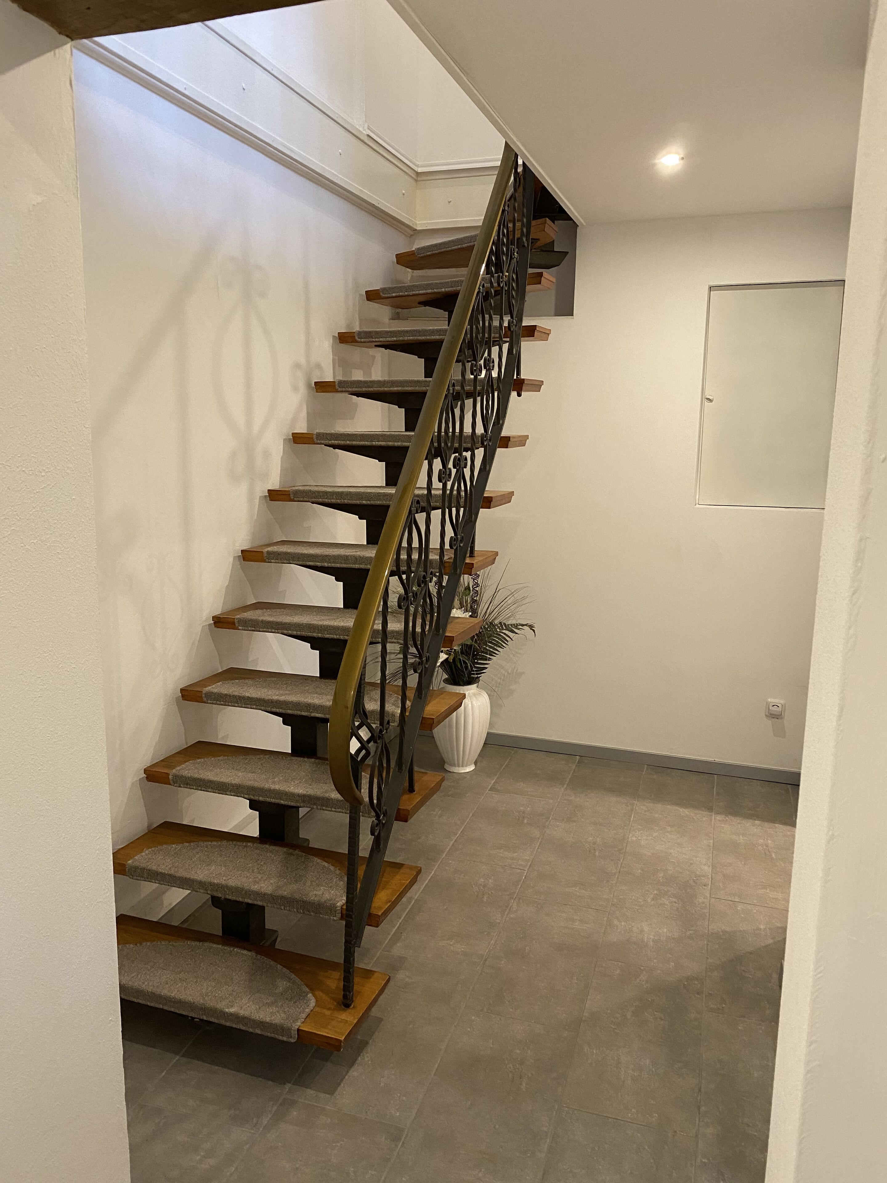 A staircase with a metal railing, wooden steps, and a white wall.