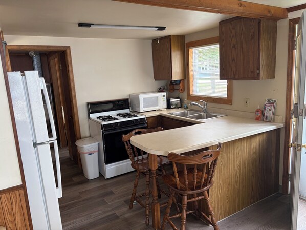 A compact kitchen with a stove, microwave, sink, and wooden cabinets.