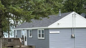 A small, single-story cottage with a nameplate reading 'Bay View Cottage.' It features a front porch with a wooden deck and a satellite dish on the roof. - Waterfront 2 b.r. Bay View Cottage/sunsets/wineries/lighthouses/beaches/fishing (Sturgeon Bay)