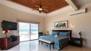 Een slaapkamer met een groot bed, een televisie, een bankje, een bureau en uitzicht op het strand.