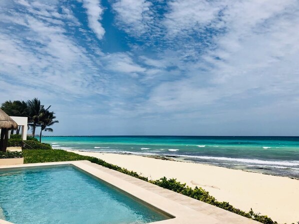 A pool adjacent to a beach with clear skies.