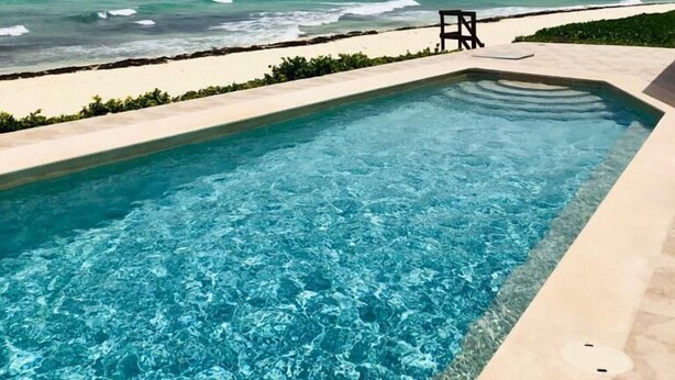 Een zwembad met helderblauw water, een zandstrand en de oceaan op de achtergrond.