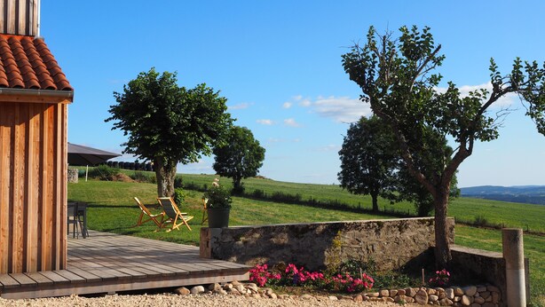 A wooden building with a tiled roof, a wooden deck, and a stone wall with a flower bed. - The ash trees of Augustus (Clavières)