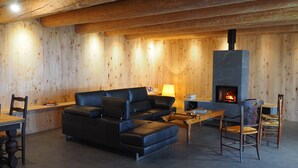 A cozy living room with a black leather sofa, wooden walls, a fireplace, and a dining area with a table and chairs. - The ash trees of Augustus (Clavières)
