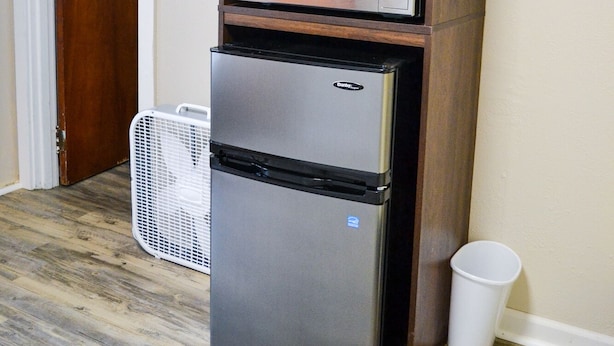 A compact kitchen with a built-in microwave and refrigerator, a small laundry basket, and a door with a metal handle.