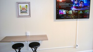 A room with a flat-screen TV mounted on the wall displaying a video game, a framed picture on the wall, and a wooden table with two black stools.