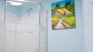 A bathroom with a glass shower enclosure, a white toilet, and a colorful landscape painting on the wall.
