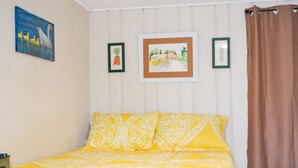 A bedroom with a bed, yellow patterned bedding, a brown curtain, and two framed pictures on the wall.