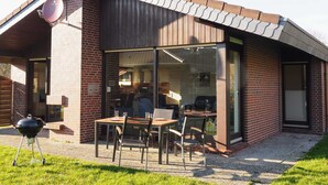 Ein modernes Haus mit einer Terrassenanlage, inklusive Grill, Sitzgelegenheit und Glastür zu einem Innenbereich.