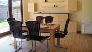 Ein Essbereich mit einem Holztisch, vier Korbstühlen und einer Küche im Hintergrund.