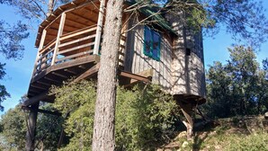 A treehouse with a wooden deck and a small window, surrounded by trees and a clear sky. - Mansion - Souvignargues (Souvignargues)