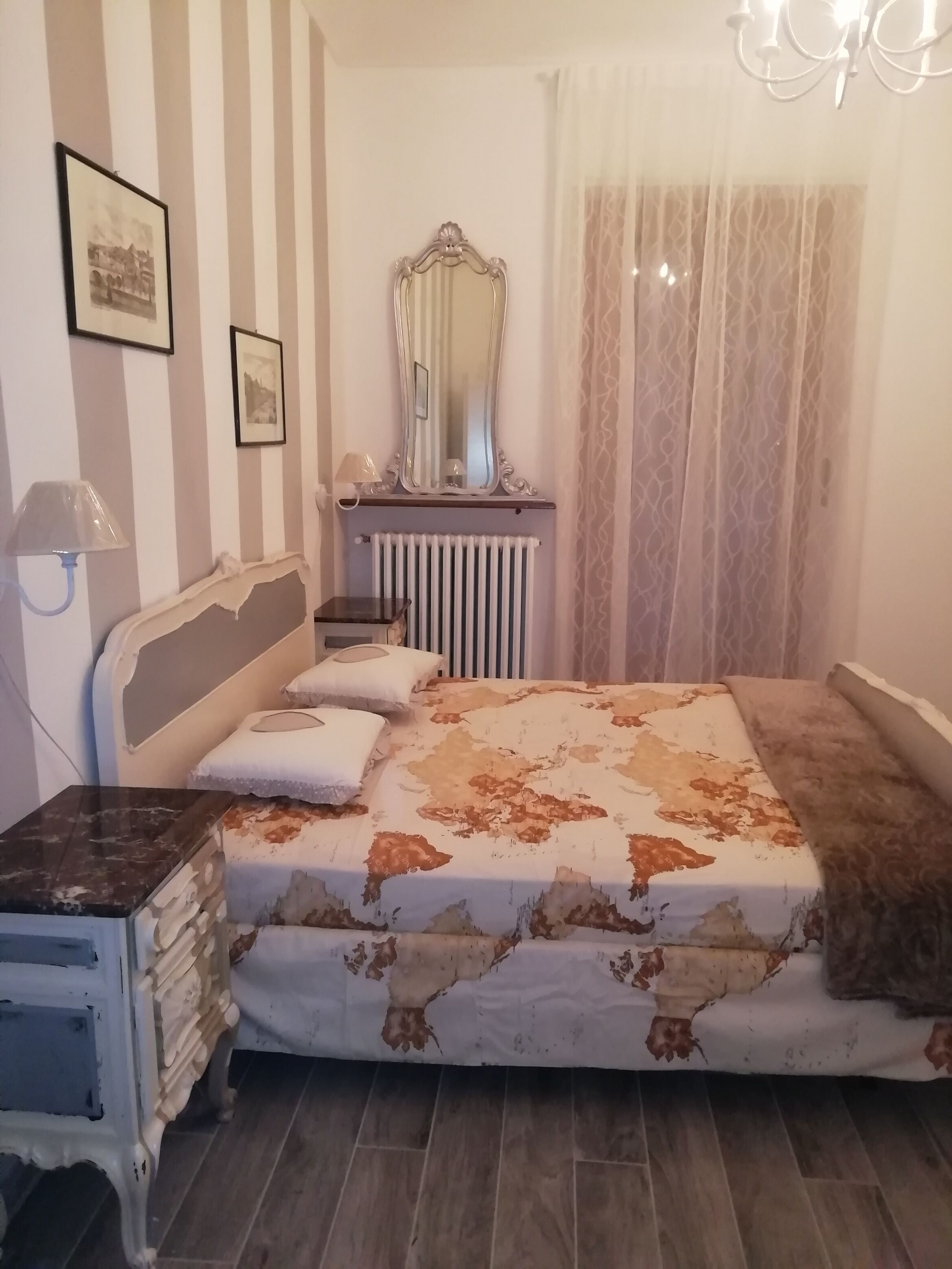 A bedroom with a bed, a dresser, a mirror, a radiator, and a chandelier.