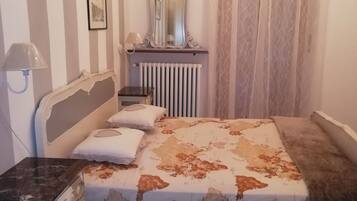 A bedroom with a bed, a dresser, a mirror, a radiator, and a chandelier.