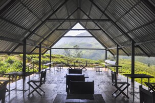 Un área de estar al aire libre con techado, con mesas y sillas, con vistas a un valle exuberante.