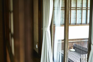 Vista a través de una ventana con cortinas, un balcón de madera y una barandilla.