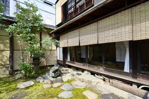 Un edificio japonés tradicional con fachada de madera, amplias puertas correderas y un pequeño jardín con rocas y musgo.