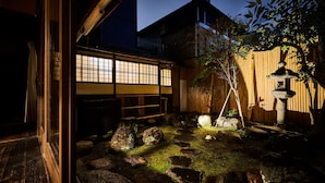 Un jardín japonés tradicional con una construcción de madera, faroles de piedra y una valla de bambú.