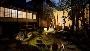 Un jardín japonés tradicional con cerca de madera, un farol de piedra y un árbol de bambú.