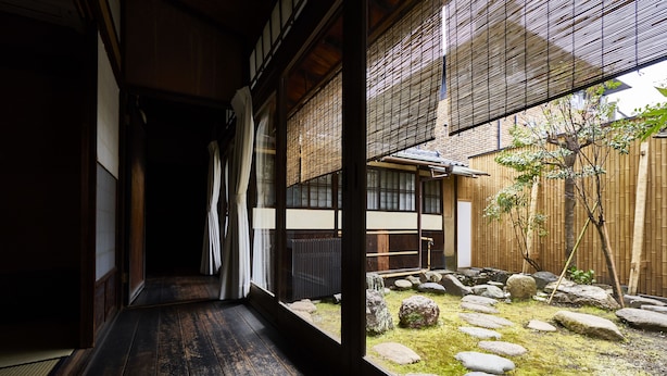 Un interior japonés tradicional con suelo de tatami, puertas correderas y vistas a un jardín con rocas y una valla de bambú.