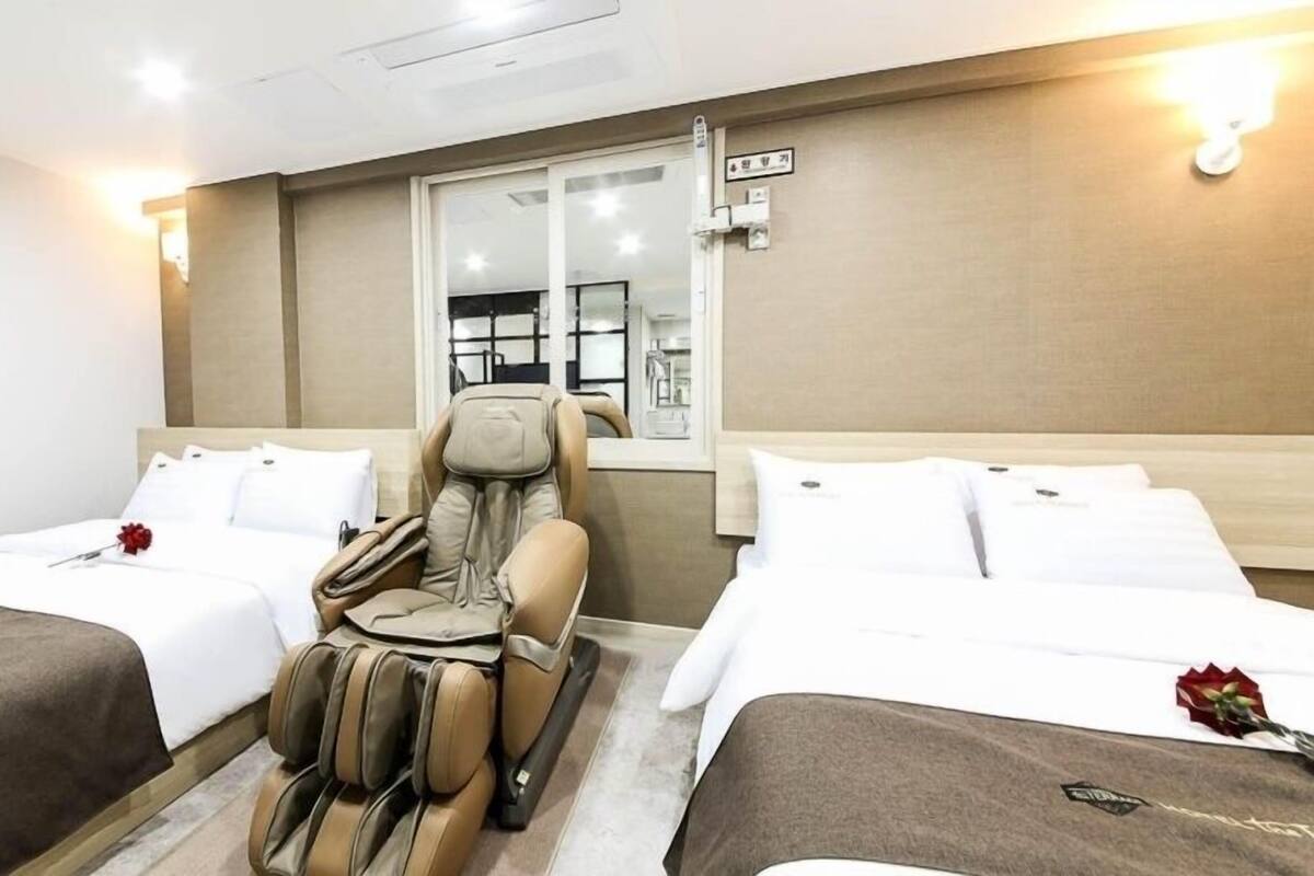 A hotel room with two beds, a massage chair, a large mirror, and a minibar.