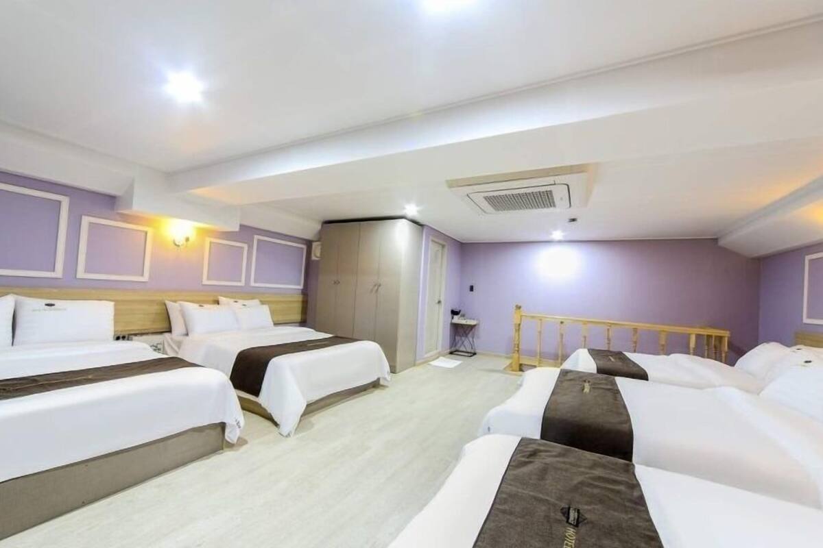 A hotel room with two single beds, a wardrobe, a desk, and a small seating area.
