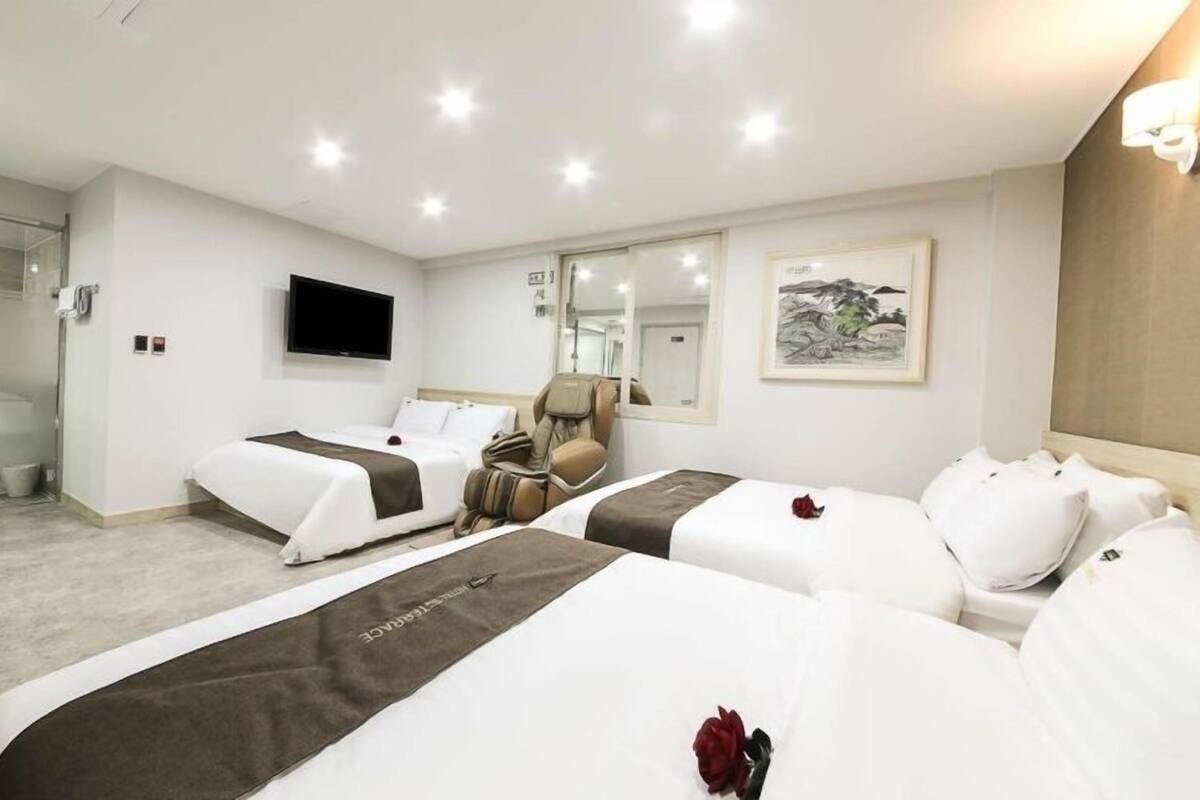 A hotel room with two beds, a massage chair, a TV, and a shower area.