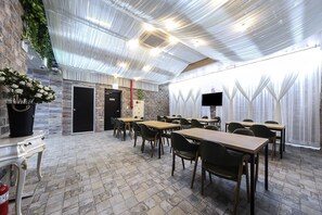 Un salón de conferencias con mesas y sillas, una pared de ladrillo y un amplio ventanal con cortinas.