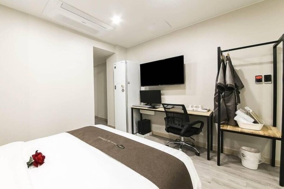 A hotel room with a bed, a desk with a computer, a TV, and a coat rack.