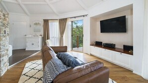 Una sala moderna con un sofá de cuero marrón, un televisor de pantalla plana montado en la pared y una pared de acento de piedra.