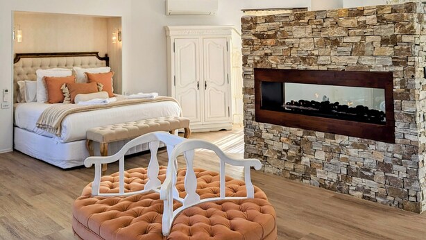 Un dormitorio con techo abovedado, chimenea de piedra, cama con cabecera y un ventanal grande.
