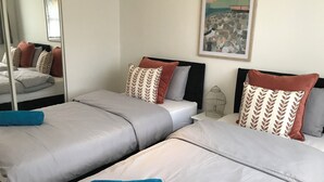 A hotel room with two beds, each with grey linens and brown patterned pillows. There is a large mirror on one wall and a painting above the bed. - Swale Corner Home from Home (Wellingborough)