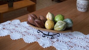 Un salon avec une table en bois, une nappe en dentelle, un canapé, une guitare, un téléviseur et un élément décoratif mural.
