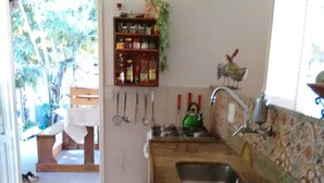 Une cuisine équipée d’un évier, d’une cuisinière et de divers ustensiles. Un chien est allongé sur le sol, près de l’entrée.