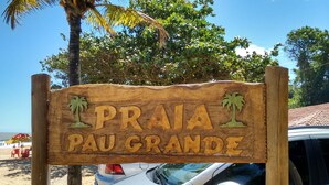 Un panneau en bois portant l’inscription « Praia Pau Grande » et orné de sculptures de palmiers.