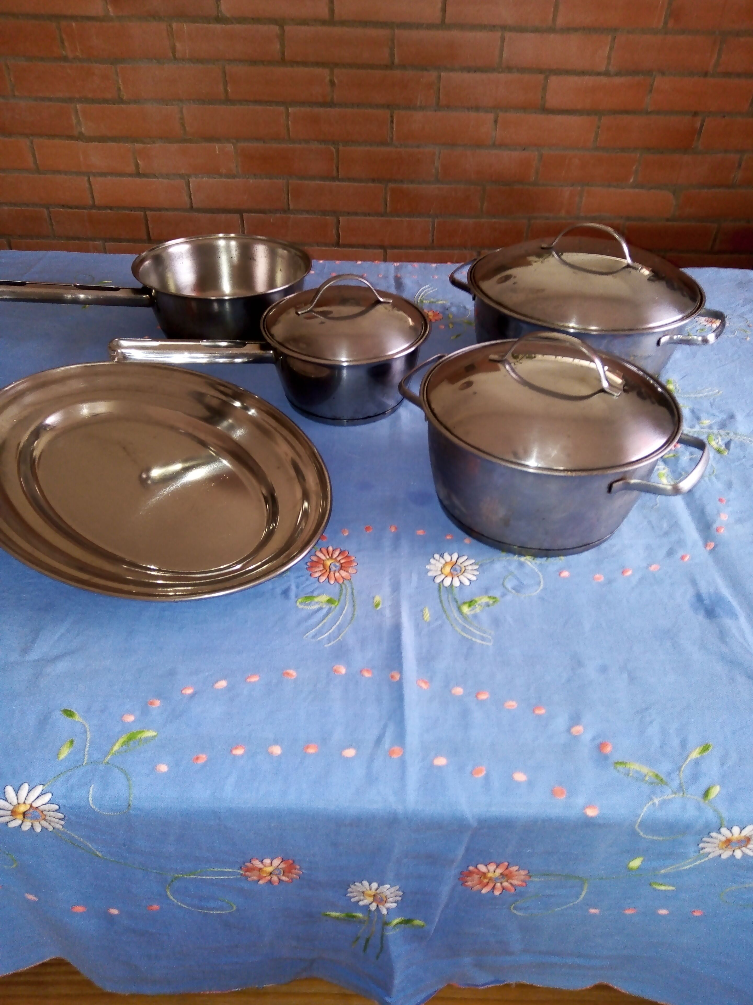 A table set with stainless steel cookware and plates on a blue tablecloth with floral embroidery.
