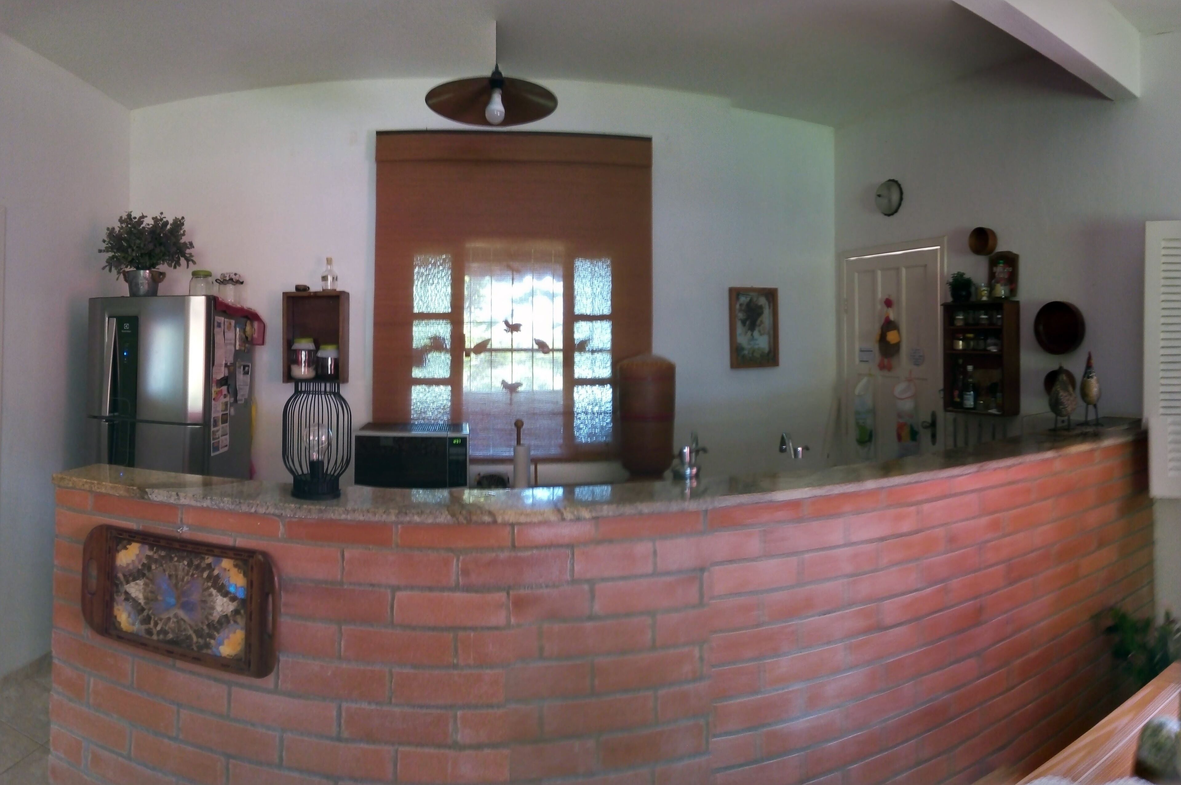 A kitchen with a brick island, a refrigerator, a microwave, and a window with blinds.