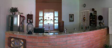 A kitchen with a brick island, a refrigerator, a microwave, and a window with blinds.