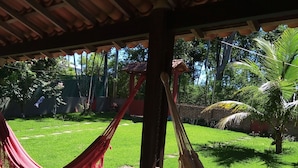 Un hamac sous une pergola en bois, avec une pelouse verdoyante et des palmiers en arrière-plan.