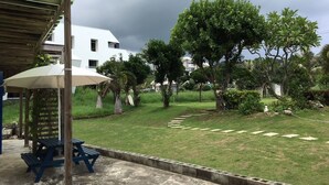 A covered outdoor area with a picnic table and umbrella, surrounded by a grassy lawn and trees, with a building in the background. - Peanut House (Hengchun)