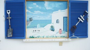 A framed artwork depicting a coastal scene with a house, a shovel, and gardening tools. - Peanut House (Hengchun)