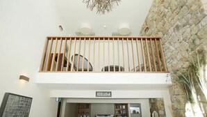A modern interior with a stone wall, a wooden balcony railing, and a television on a wooden stand.