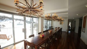 A spacious dining area with a long wooden table and chairs, large windows offering a view of a snowy landscape, and a unique chandelier.