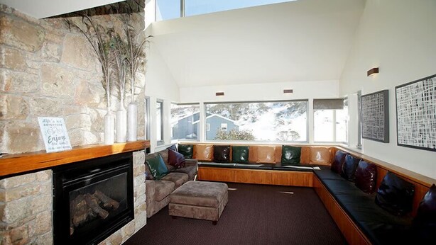 A cozy living room with a stone fireplace, a built-in bench with cushions, and large windows offering a view of the outside.
