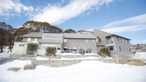 A two-story building with a stone foundation, a metal roof, and a large front entrance.