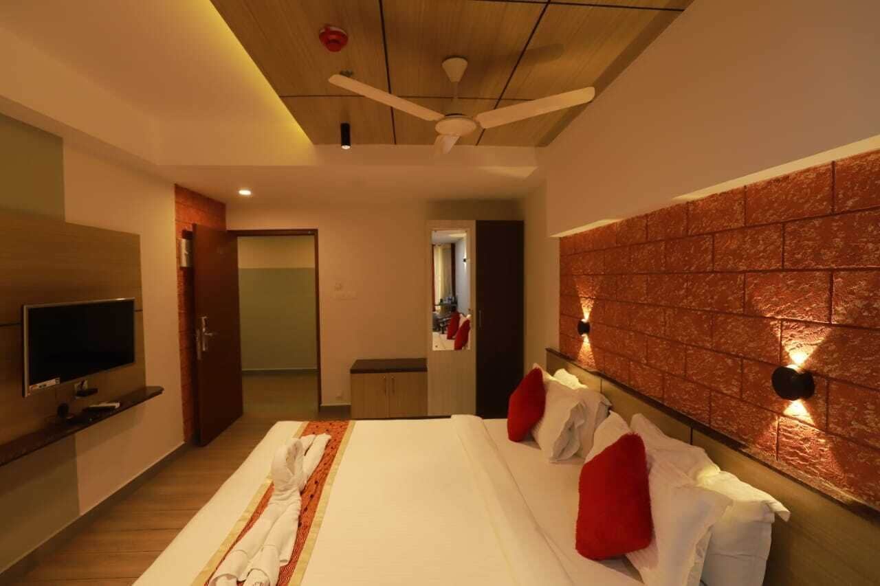 Habitación de hotel moderna con una cama grande, un televisor de pantalla plana, un ventilador de techo y una pared decorativa con diseño de ladrillo.